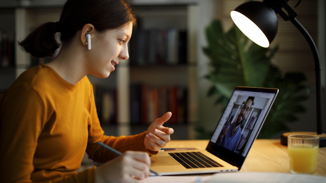 Smiling teenage girl with bluetooth headphones having video call on laptop computer at home 