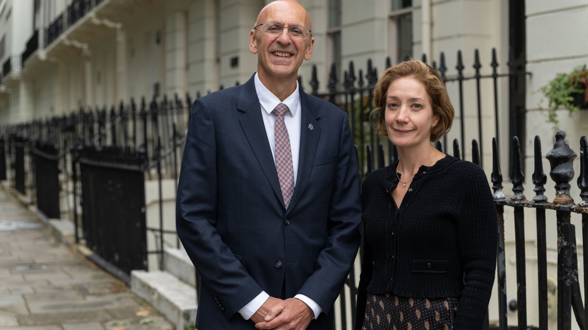 Malcolm Press and Vivienne Stern smiling in front of a row of white houses