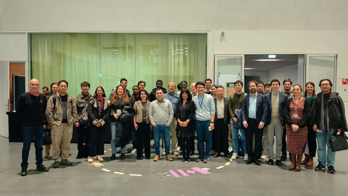A large group of workshop attendees pose for a photo in a room at the University of Paris-Saclay