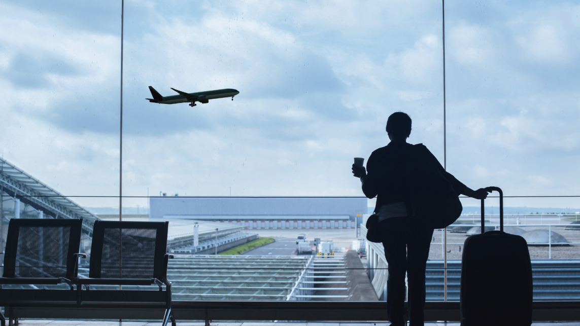 A person in an aiport watching over the window as plans depart