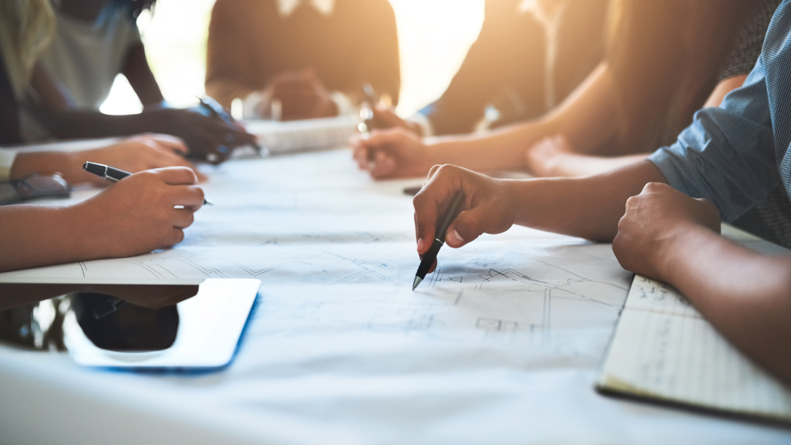 Close-up of a group of people collaborating by making notes together on a large sheet of paper.