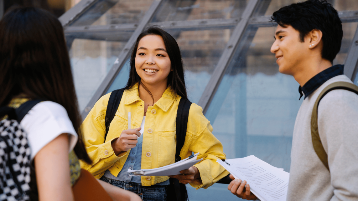 Three students talking to each other, holding study materials