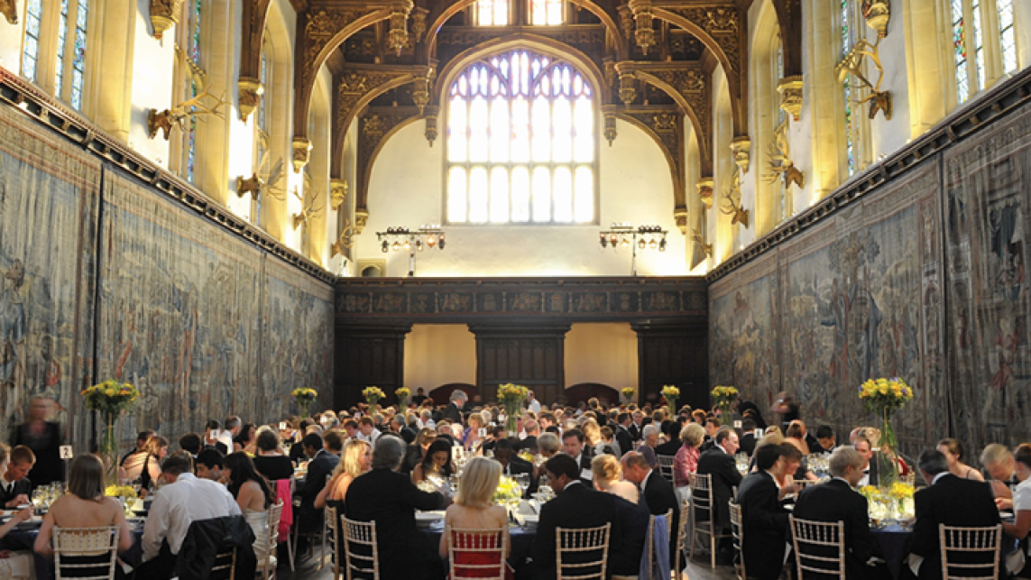 a group of people dining at round tables in a grand setting 