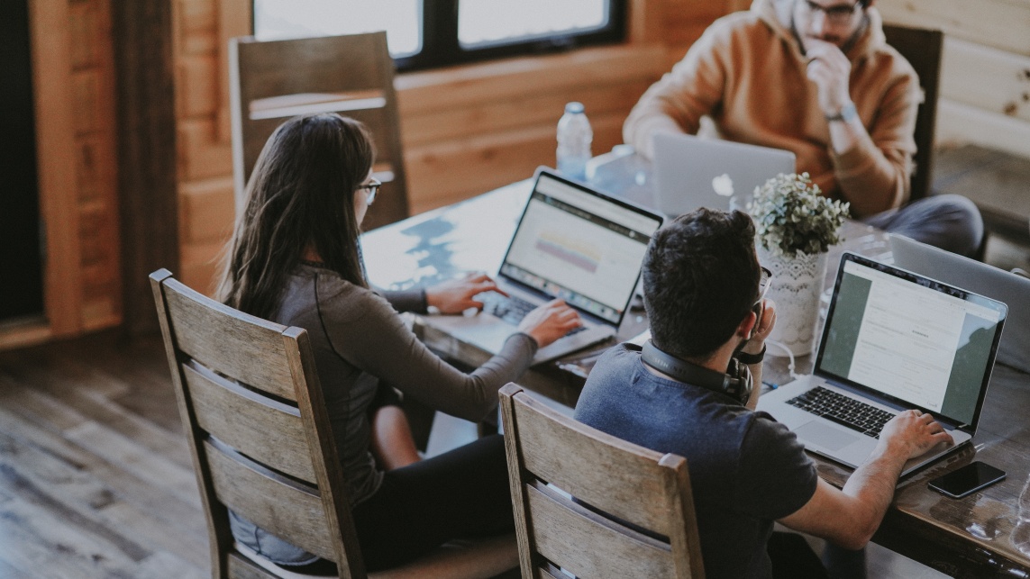 A project team, sat around a table (three people in total) looking at laptop screens