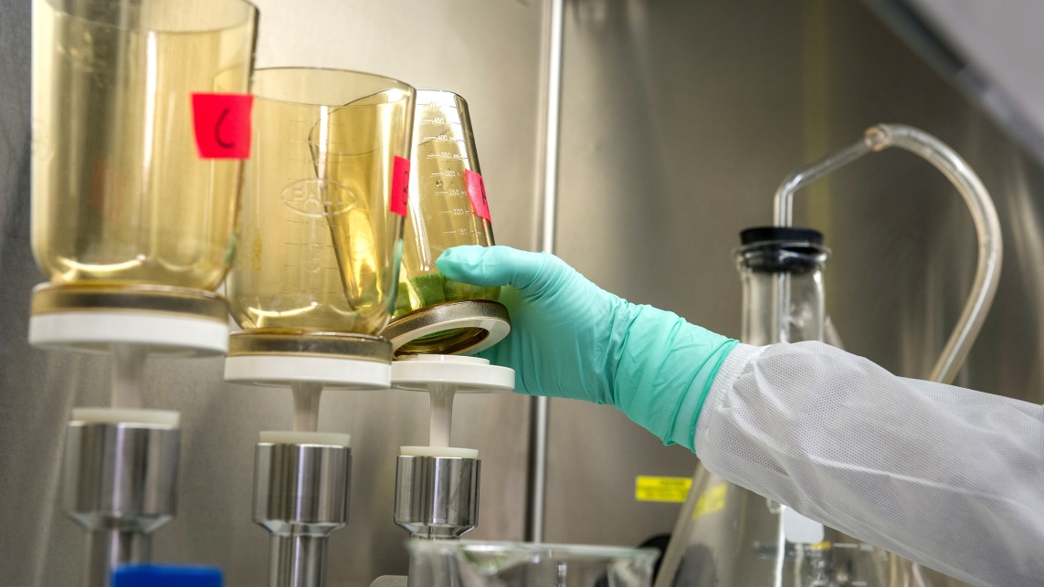 A person in lab equipment reaching for a test beaker