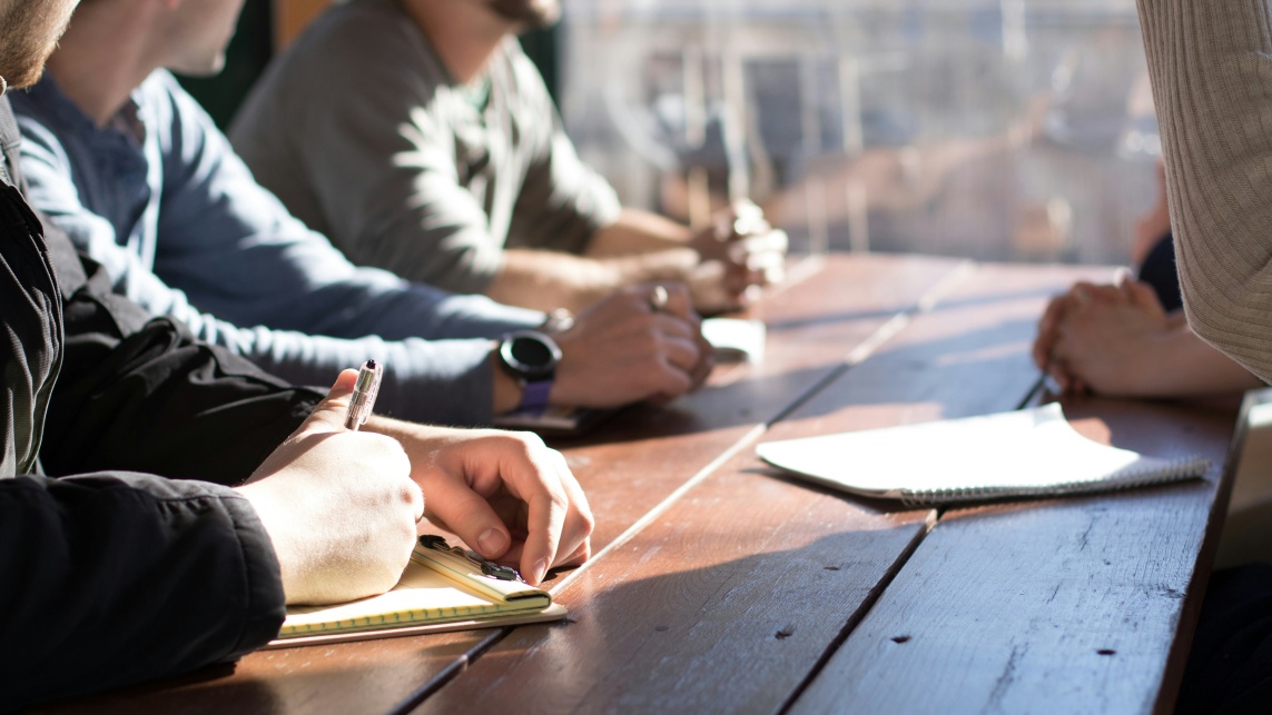 People working on a desk, taking notes and discussing with each other