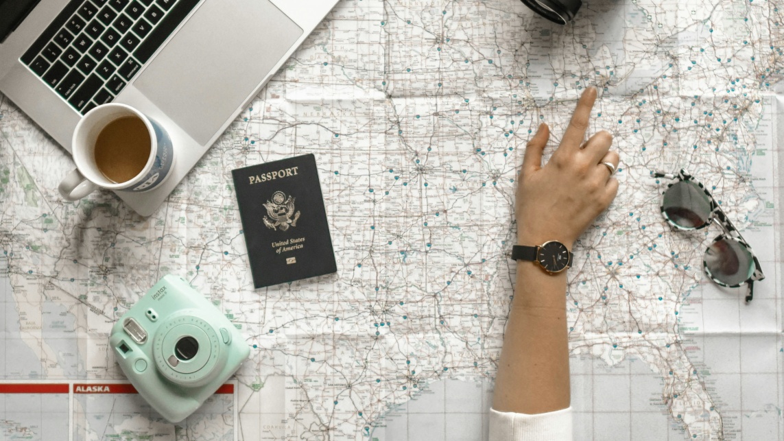 Person looking at a map with a passport, camera, sunglasses and laptop 