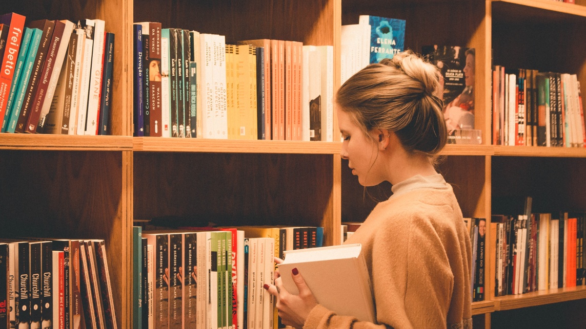 A person stands in a library, facing the books