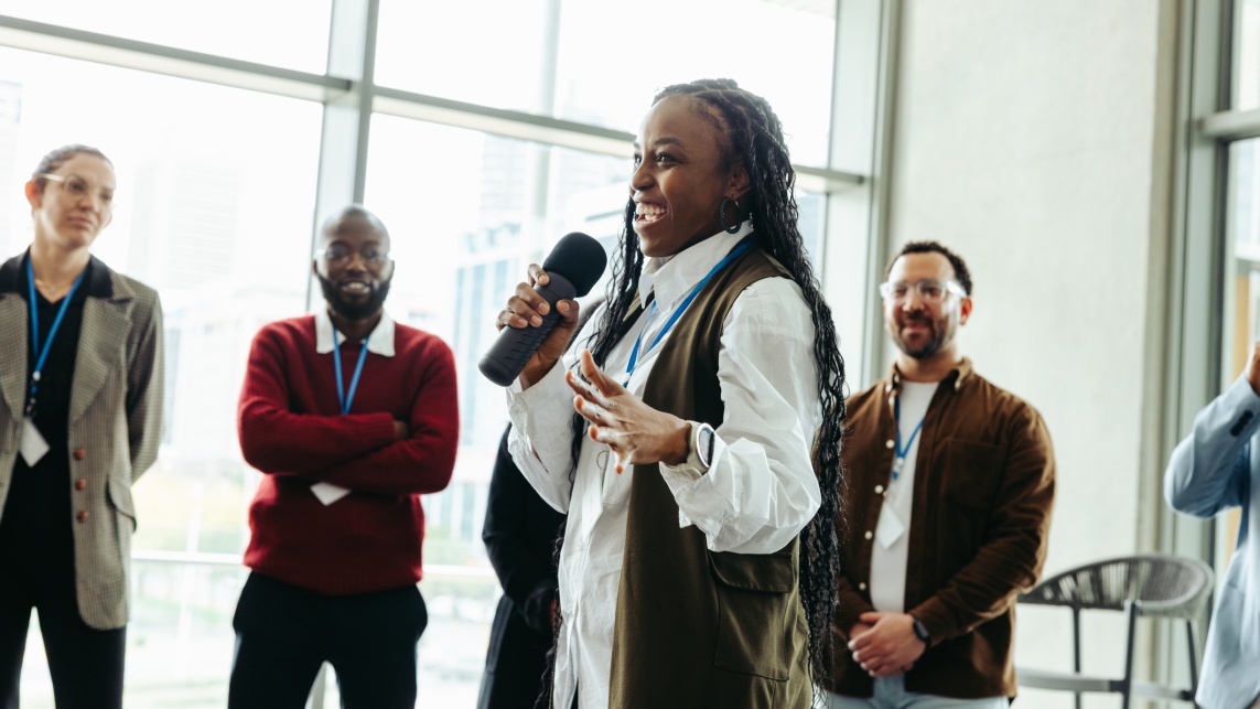 Woman speaking into a microphone surrounded by a crowd of people listening.