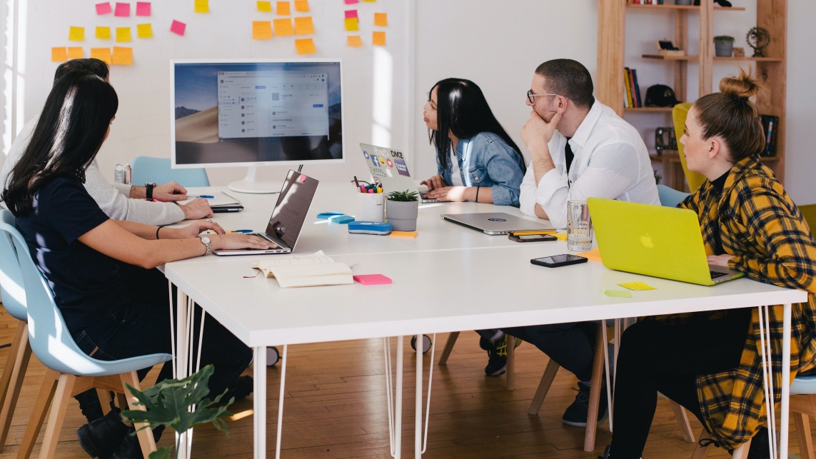 People around table with laptops looking towards sticky notes on whiteboard 