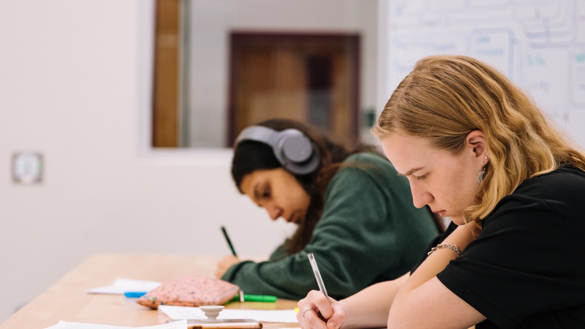 two students making notes, one with headphones on