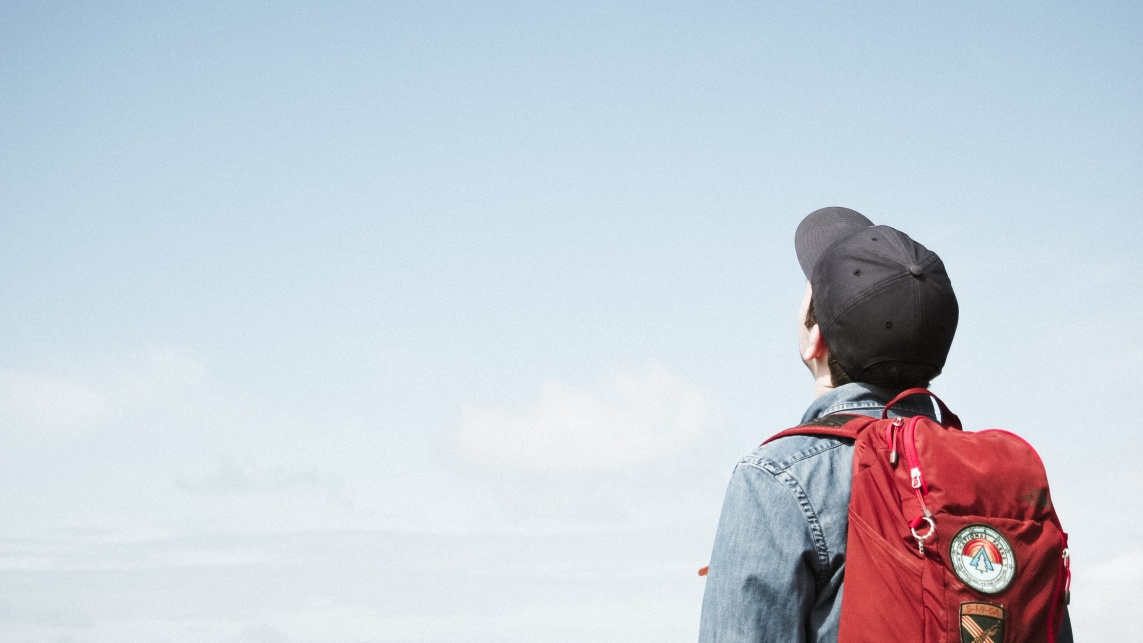 Back of student with rucksack and hat looking up into sky 