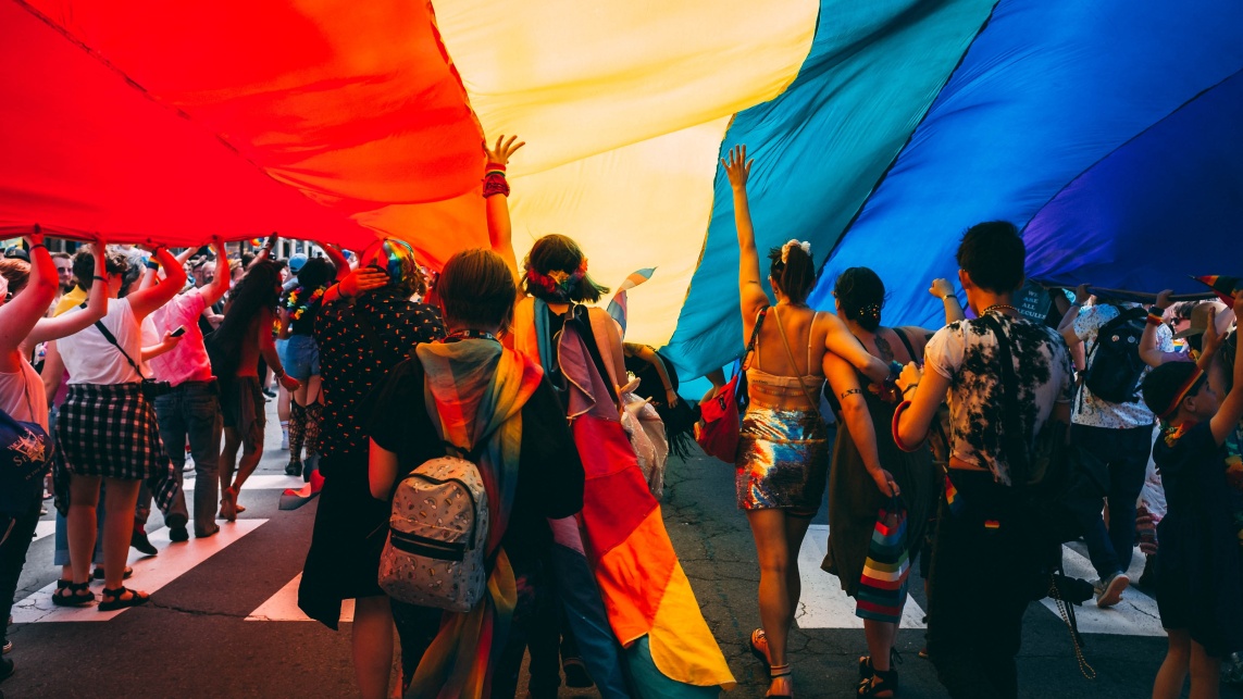 A group of people underneath a large rainbow flag