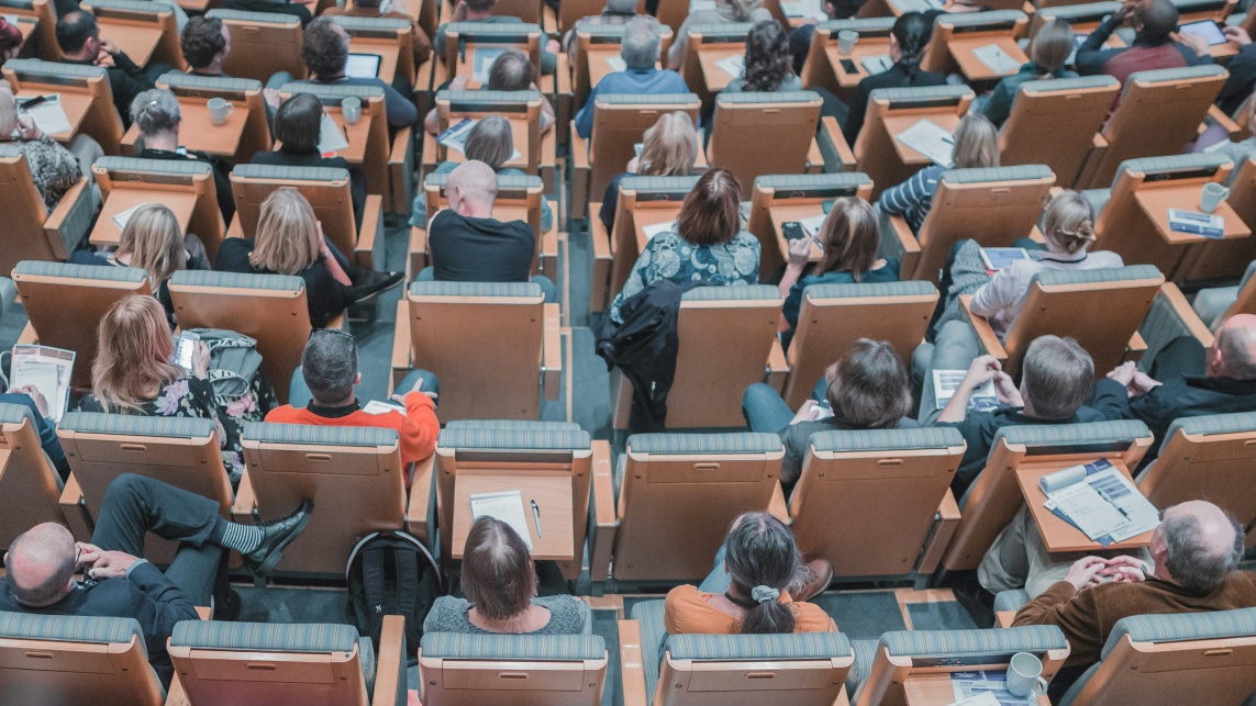 An aerial view of a lecture hall ,with students listening to a lecture, sat on their seats with laptops and notebooks in front of them