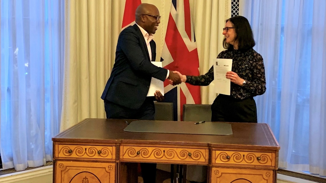 This is an image of Celia Partridge and Charles Achampong shaking hands after the agreement was signed and renewed. Celia is holding the document in her other hand.