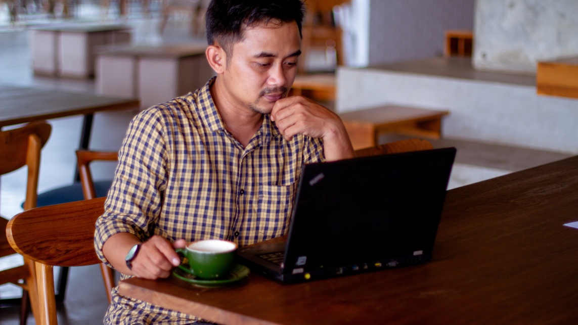 Man at table with open laptop and coffee