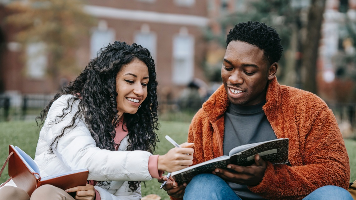 Man and woman sitting outside and smiling while doing work together