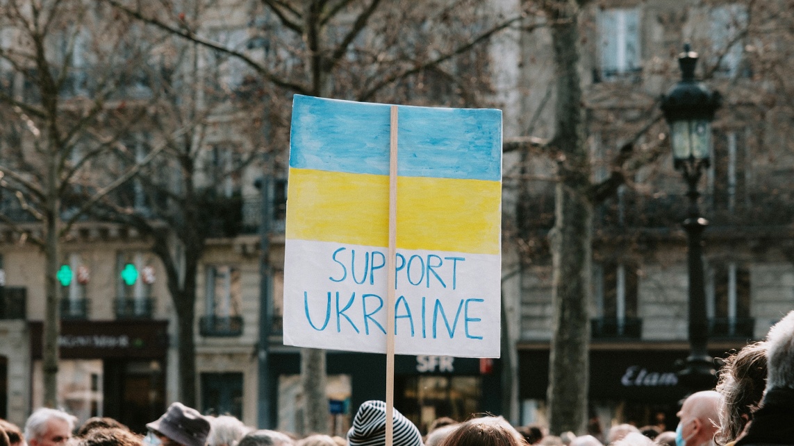 Handmade placard with Ukrainian flag and 'Stop Ukraine' written in capital letters, being held by a protester in a crowd