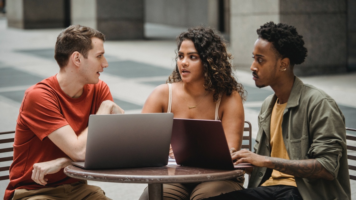 Three students doing work together using laptops at a cafe