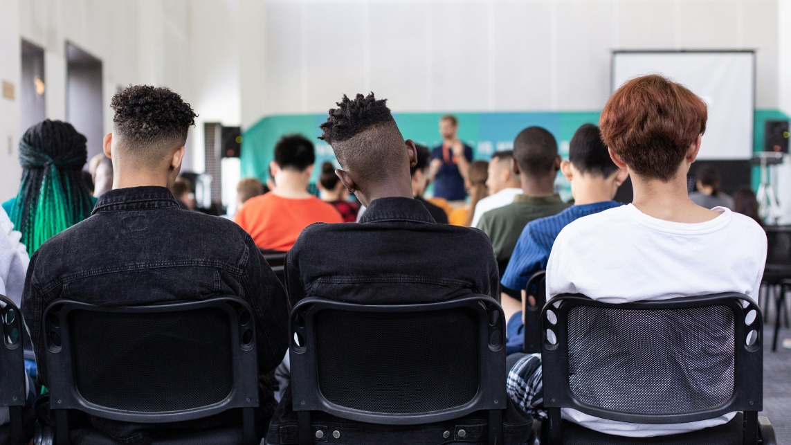 Three people sat on chairs at an event listening to a speaker