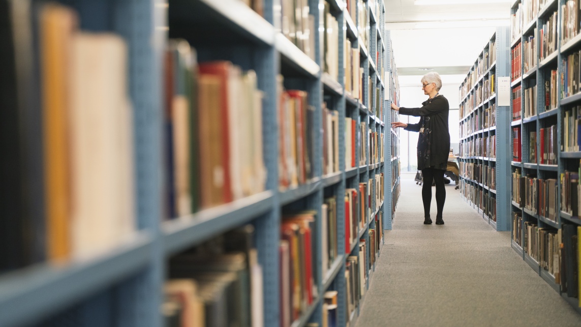 A woman browses bookshelves in a university library