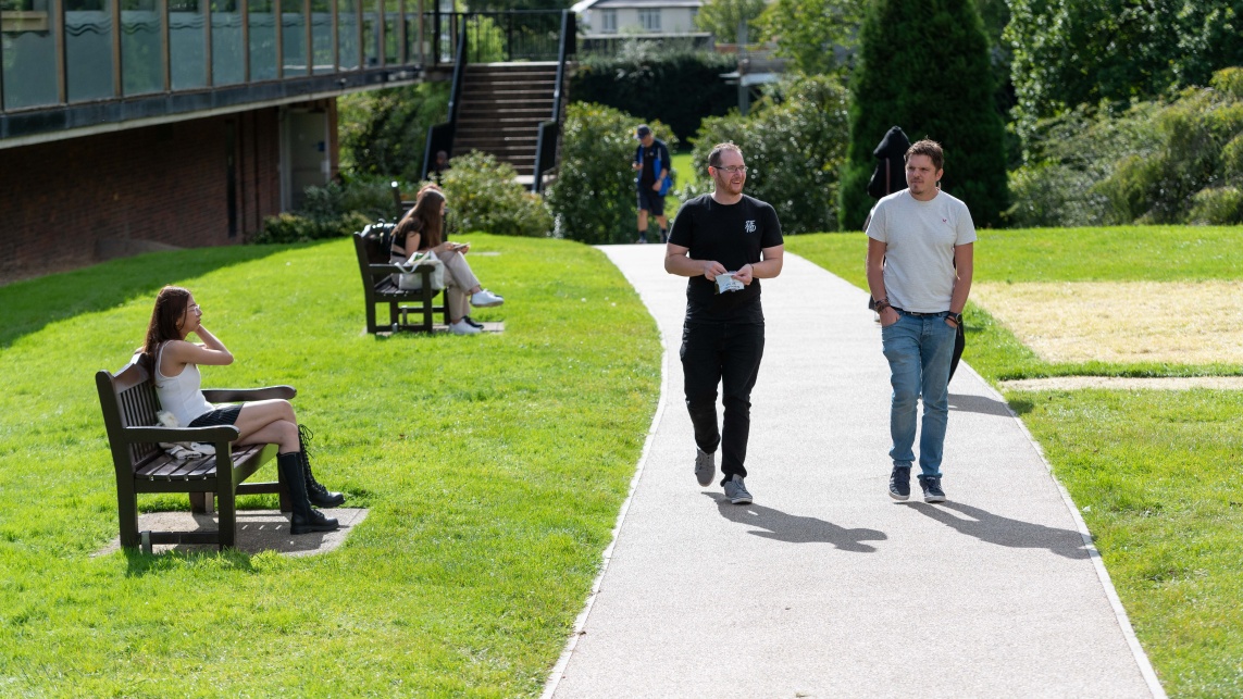 Students and staff mingle outside in a leafy university campus