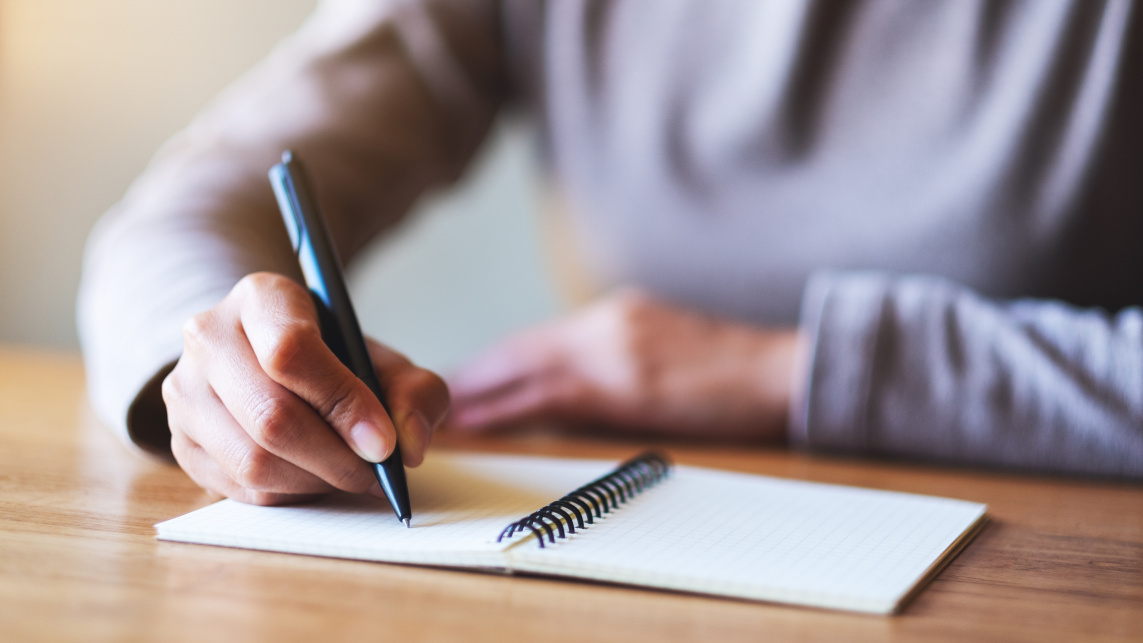 A person writing in a notebook at a desk.