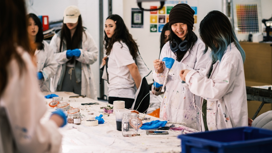Students wearing white painter's jackets work together in an art studio