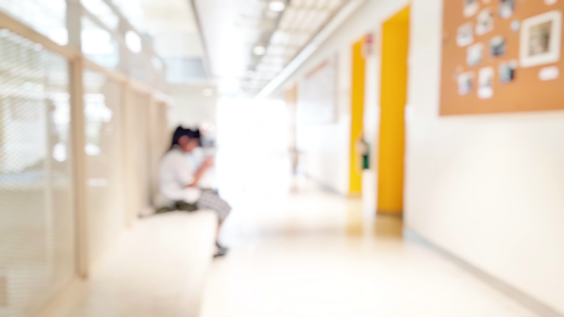 Student sitting alone in campus hallway with a phone in their hands. The image in blurred