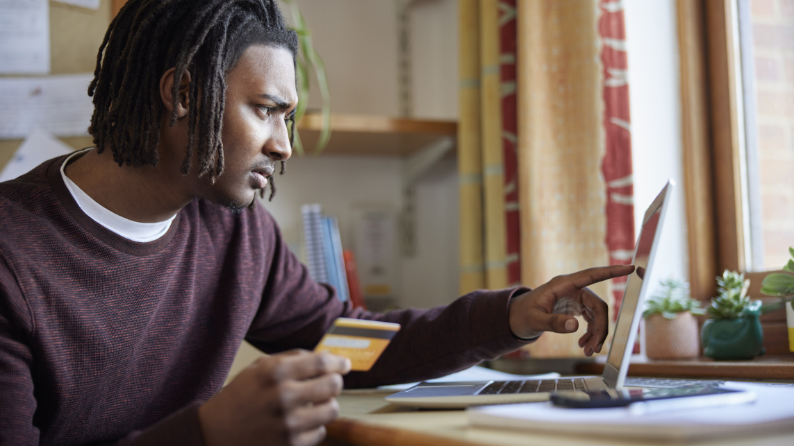 Male student sitting at a desk, holding a credit card while looking at a laptop