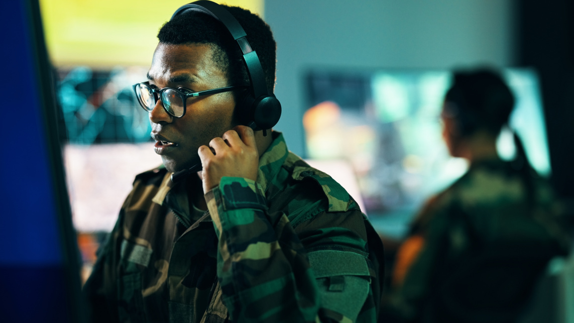 Person wearing a military uniform and headphones, looking at a computer screen