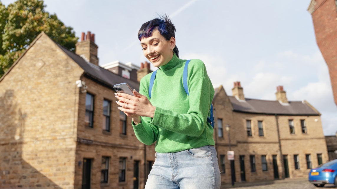 A woman looks at her phone and smiles while walking through a neighbourhood of terraced houses
