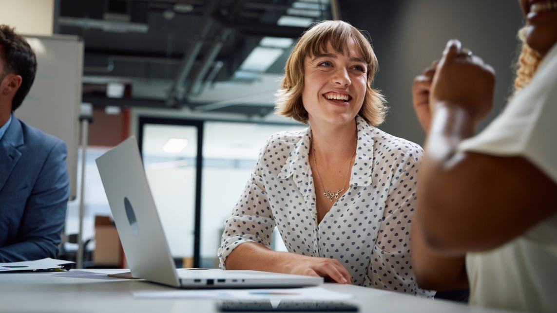 Woman smiles while speaking to colleagues in meeting in office