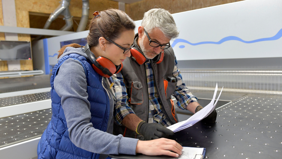 Two colleagues stand in a production workshop looking at plans together