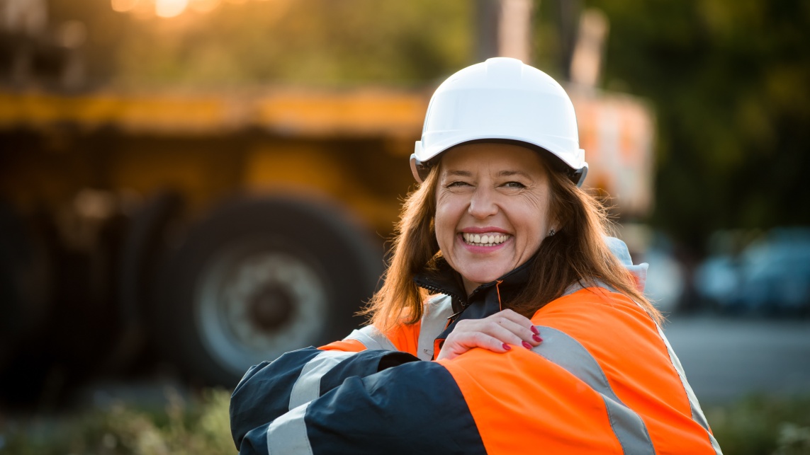 Woman wearing a high visibility jacket and helmet sitting outside and smiling