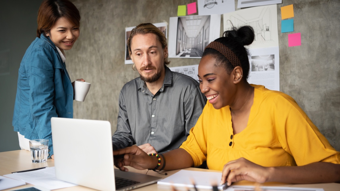 Three people crowd round a laptop to share ideas