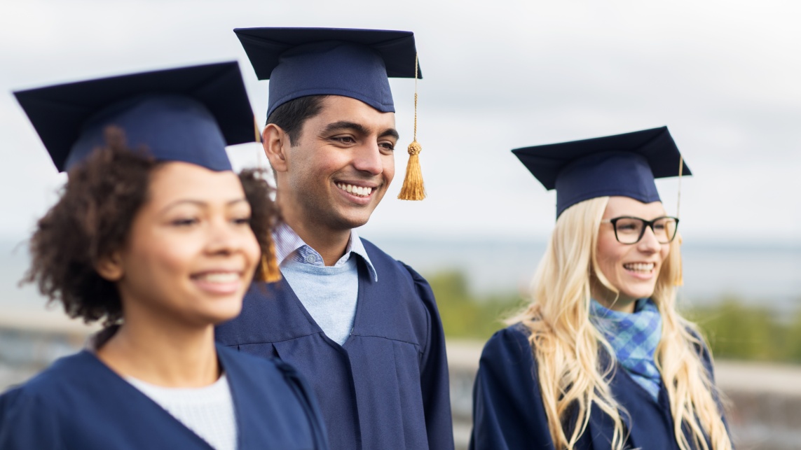 Three students walking outside, smiling in graduation gowns 