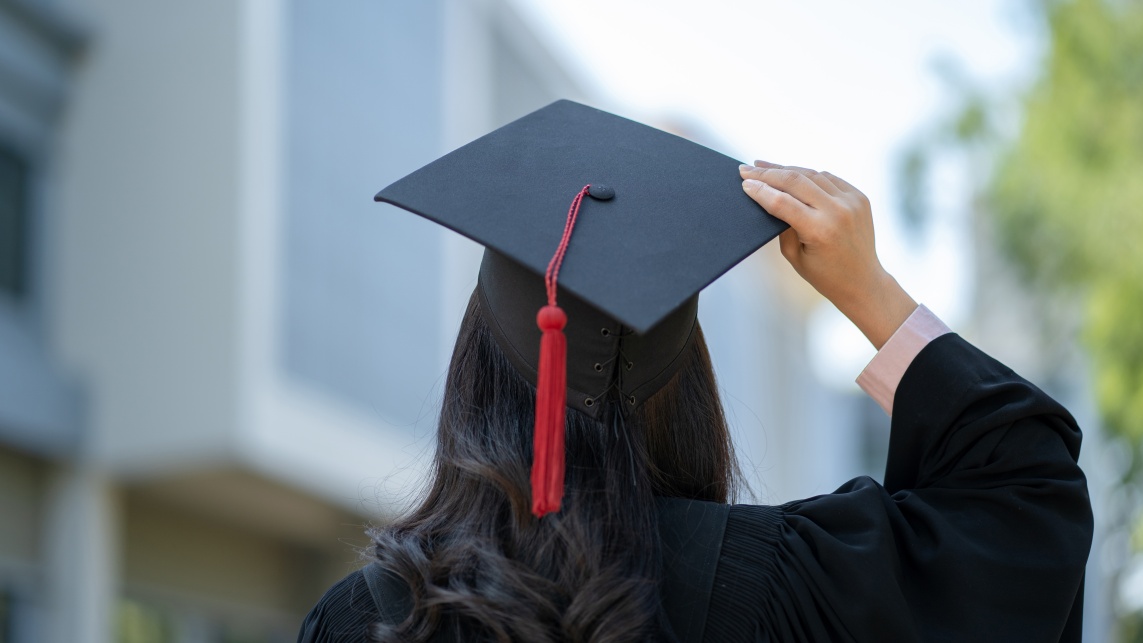 A student wearing a graduation cap walking through their campus seen from behind