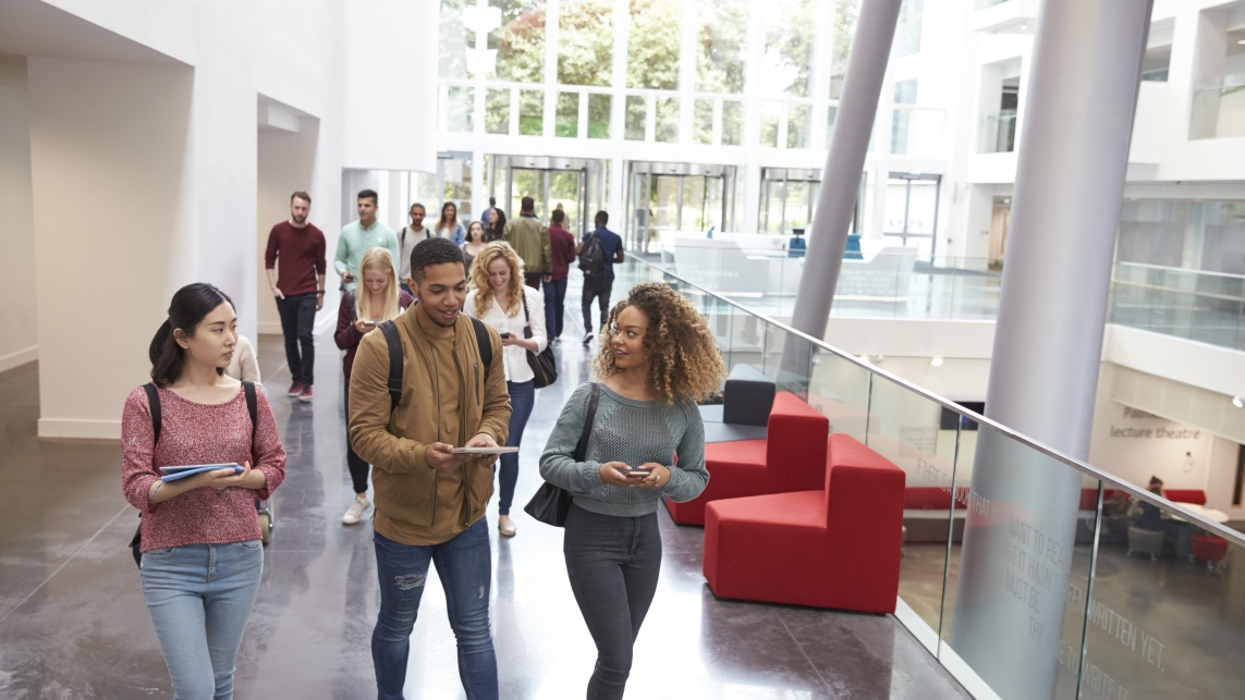 Students walking and talking using their phones in a university atrium.