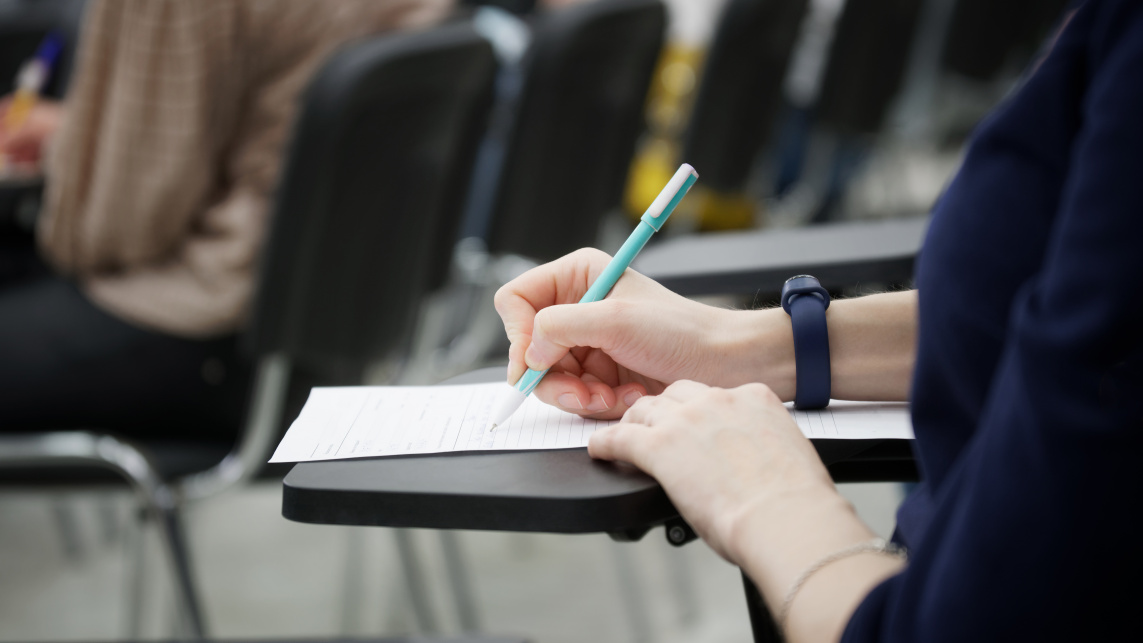 A student completes an exam paper in an exam hall