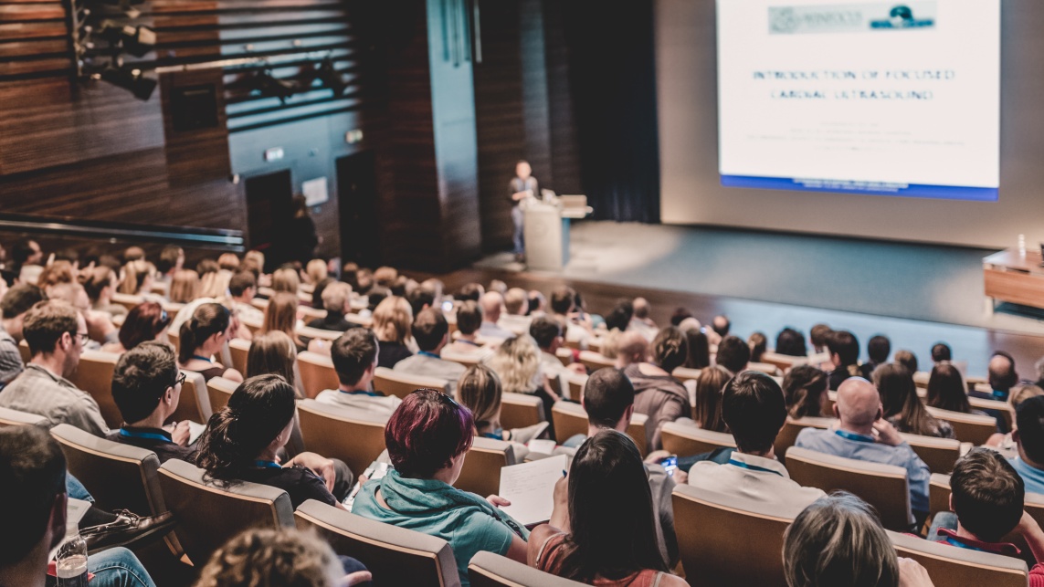 A lecturer delivering a lecture to a lecture room full of students through a digital presentation. 