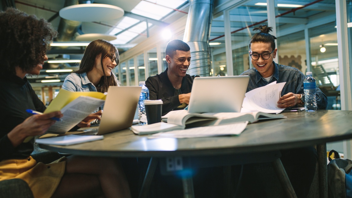 A group of cheerful students study together around a table 