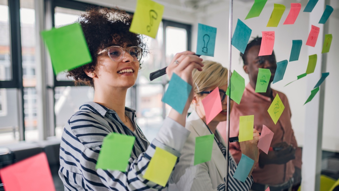 Team of three writing ideas on colourful sticky notes on a glass wall