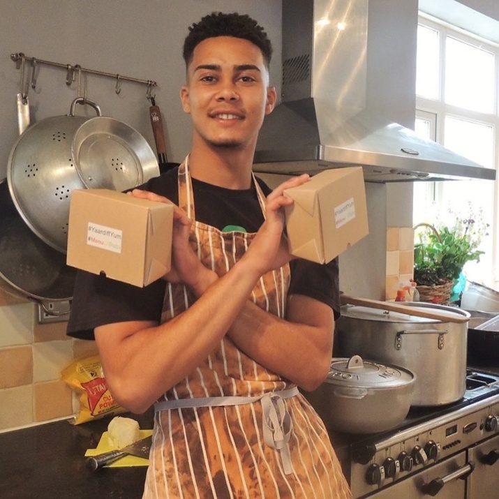 Floyd in his Kitchen with crossed arms holding two food delivery boxes