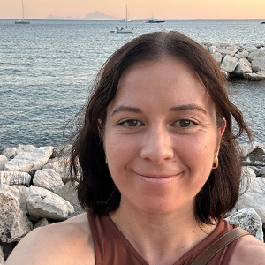 UUK staff member Chloe Brant standing in front of the ocean wearing a brown top.
