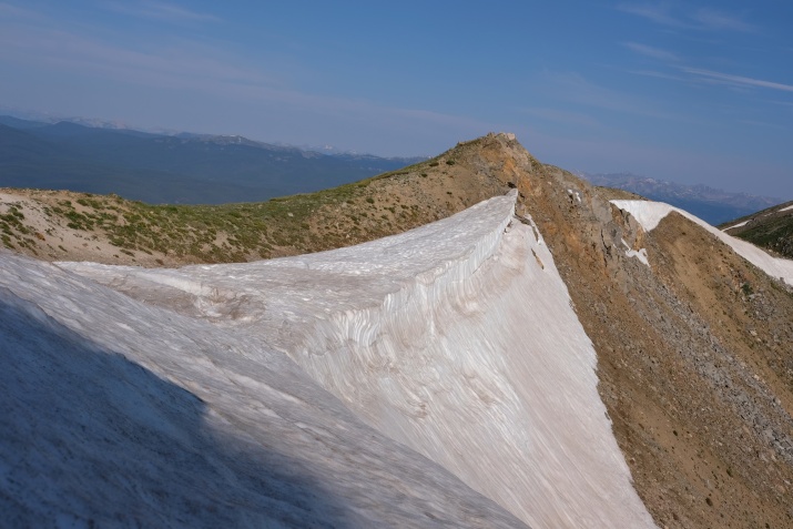 View from the top of a mountain on the Colorado Trail. The mountain is white and brown against a blue sky