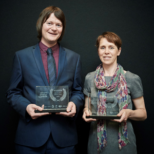 MyWay Digital Health co-founders Dr Debbie Wake and Scott Cunningham stand in front of a black background. They are both holding award statues.