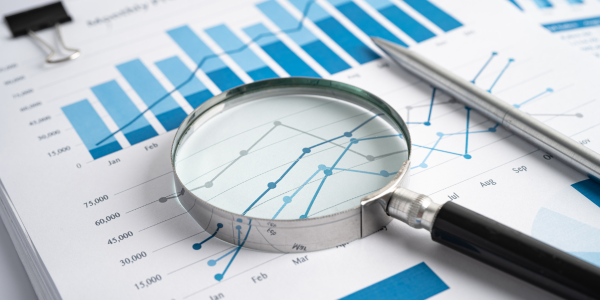 Sheet of paper displaying two graphs, with a magnifying glass on top, representing data analysis.