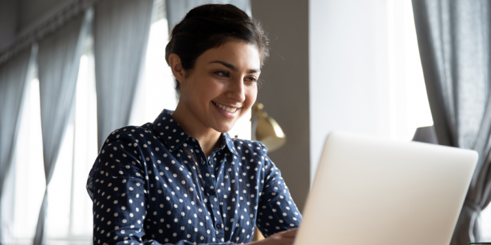 A student smiles, working on a laptop. 