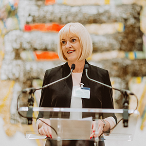 Lisa Roberts giving speech at a lecturn in front of industrial background